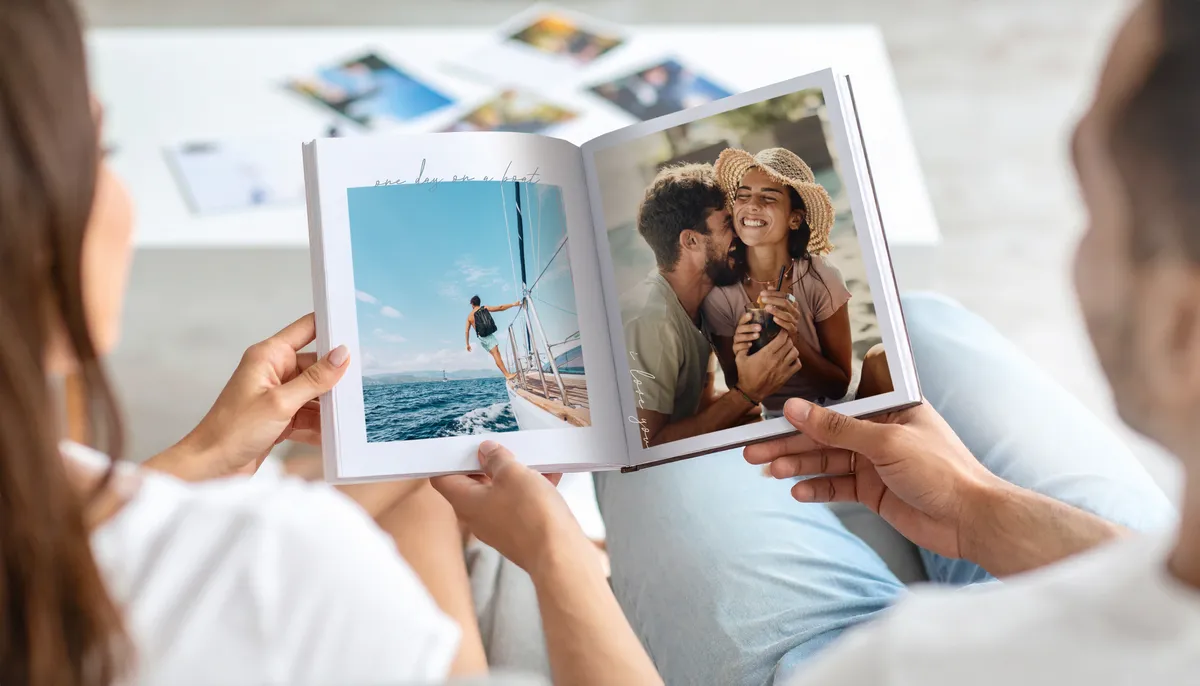 Aufgeschlagenes Urlaubsfotobuch mit Motiven eines Pärchens, das lacht und sich in den Armen liegt